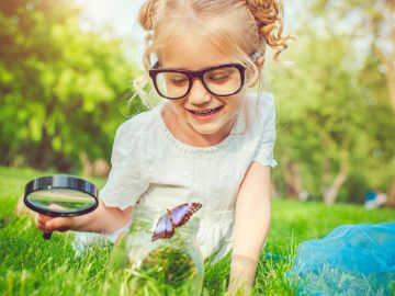 Young girl exploring nature with a magnifying glass and butterfly.