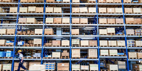 Warehouse with stacked wooden crates and a worker moving a pallet jack.