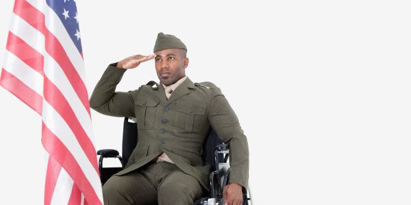 Soldier in uniform saluting while seated in a wheelchair near an American flag.