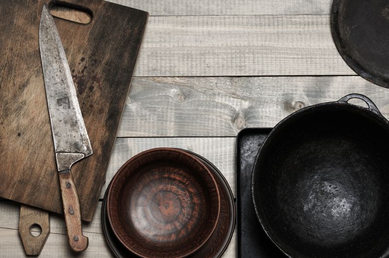 Vintage kitchen cooking utensils on rough wooden background: cutting boards, knife, crockery and cast iron cauldron. Top view point.