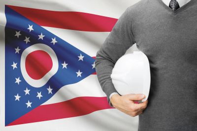 Man holding a hard hat in front of Ohio state flag.