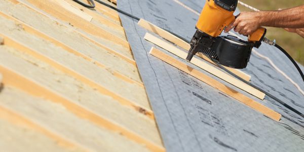 A person using an air nailer to attach the roof of a house.