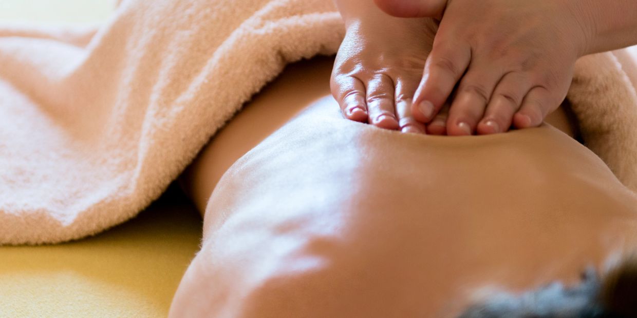 Hands giving a relaxing back massage to a person covered partially with a towel.