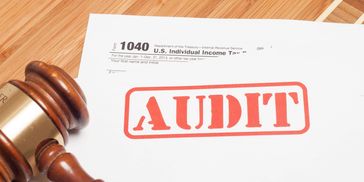 A gavel next to a tax form stamped with 'AUDIT' on a wooden surface.