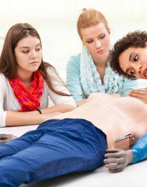 Three women practicing CPR on a training mannequin.