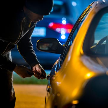 A person trying to unlock a car door at night with a tool.