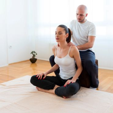 A man giving a seated woman a shoulder massage in a bright room.