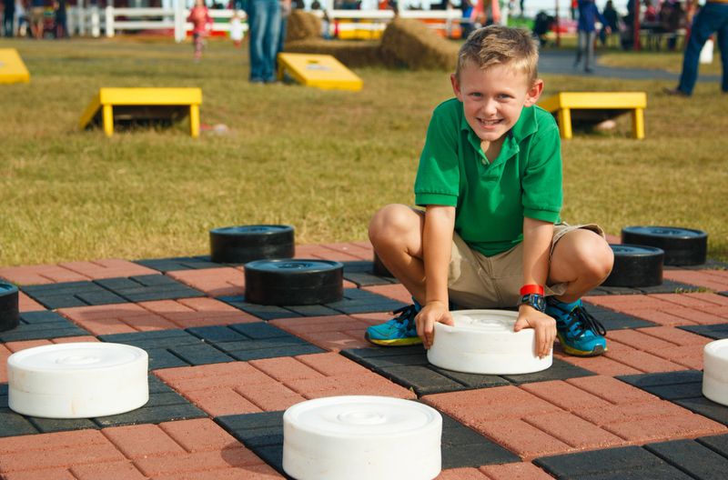 Clever young boy playing a life size checkers game outside on an autumn day at a festival.