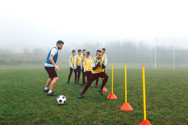 Children practicing dribbling at soccer. They are having training with their coach on foggy, cold, winter morning. They are dedicated to become a new soccer stars. Selective focus to kid in foreground.