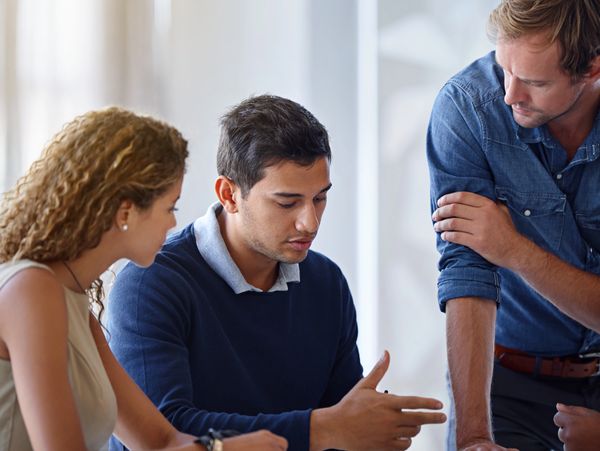 Three young professionals discussing work around a table with documents and a tablet.