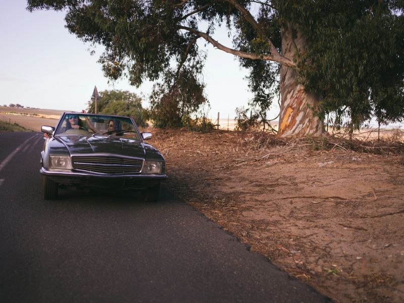 Front view of young adult hipster man driving a vintage convertible and a young adult women on the passenger seat