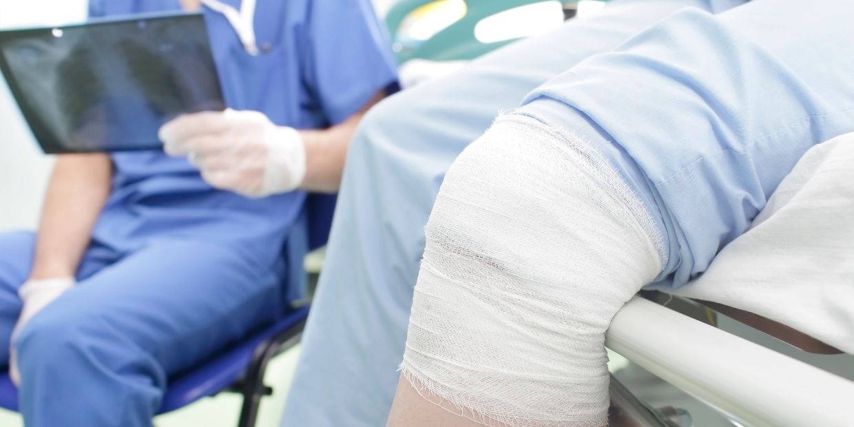 Patient with a bandaged knee in a hospital, doctor reviewing X-ray“CuraVia Concierge Nursing providing post-operative support and monitoring for a patient recovering from knee surgery.” “A patient with a freshly bandaged knee following surgery while a nurse reviews medical imaging, representing post-operative care, recovery support, and professional nursing oversight.”