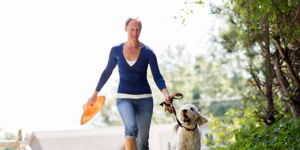 Woman joyfully walking her dog on a sunny path surrounded by greenery.