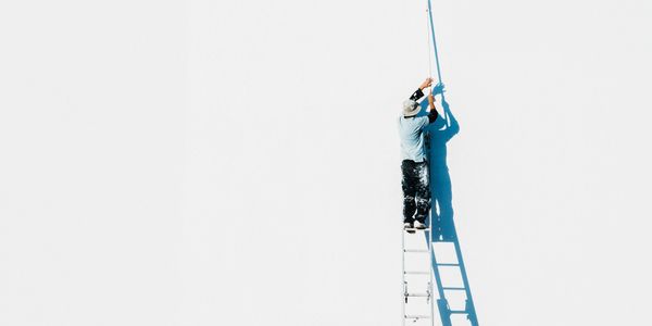 Painter on ladder painting a large white wall with a roller.