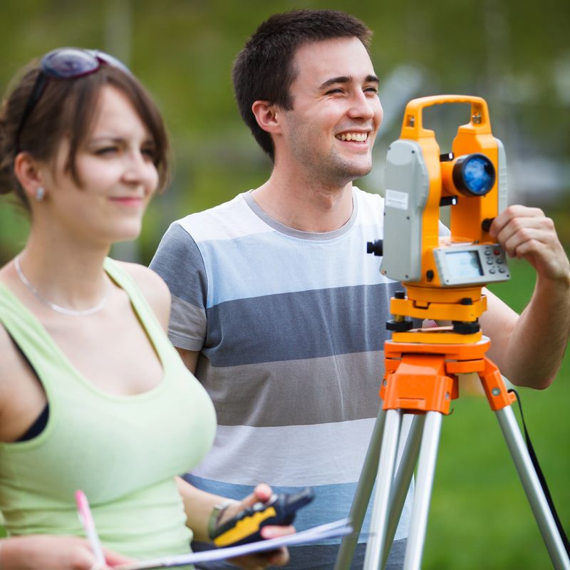 Two young land surveyors at work, measuring and mapping terrain