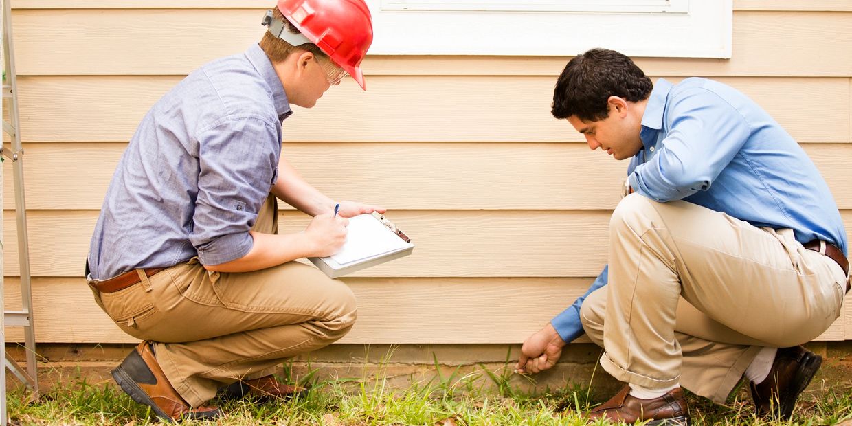 Two men inspecting the foundation of a house.