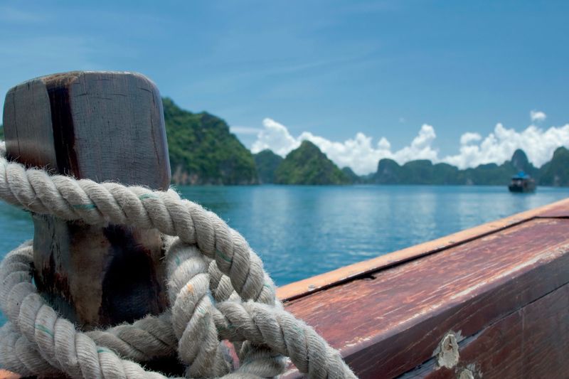 Sea site of a thick rope tied to a wooden stern in blue sky sea and mountain background