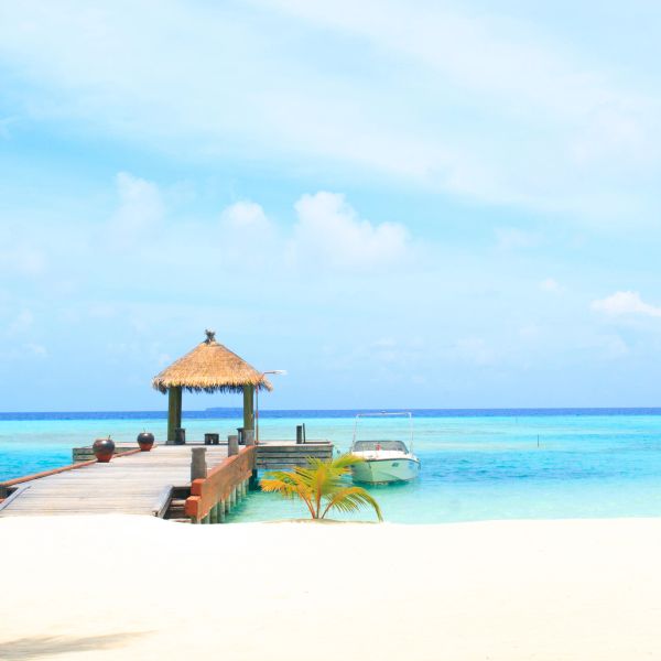 A serene beach with a wooden pier and a boat on clear blue water.