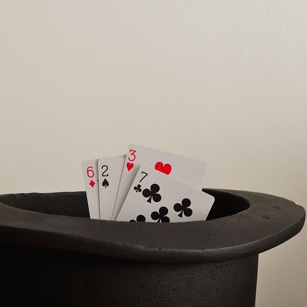 Playing cards partially inside a black magician's hat.