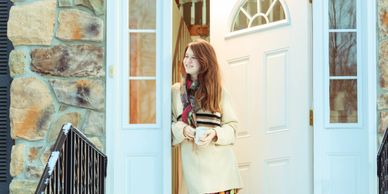 A woman stands at a white door, looking outside with a smile.