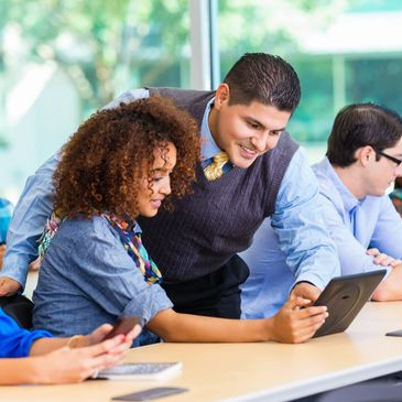 Man helping woman with tablet in a bright office setting.