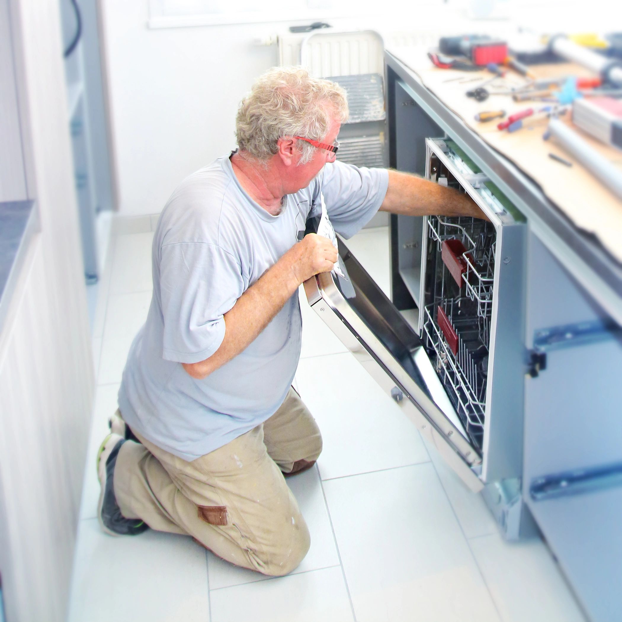 Man repairing a dishwasher in a kitchen.
