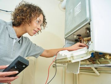 Technician inspecting and testing a boiler with a handheld device.