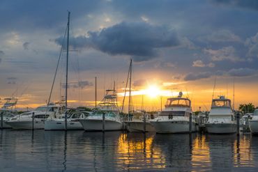 Boats docked at a marina during a vibrant sunset with colorful reflections on the water.
