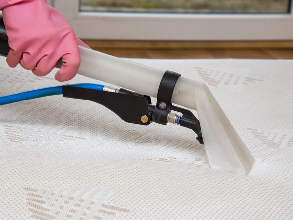 Cleaning a mattress with a vacuum tool.