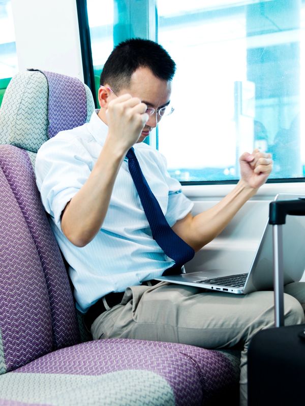 Man celebrating success while working on laptop during travel.