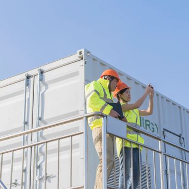 Two construction workers in safety gear inspecting a container outdoors.