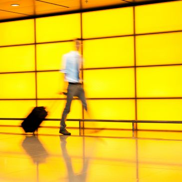 Blurred person walking with suitcase against bright yellow wall.