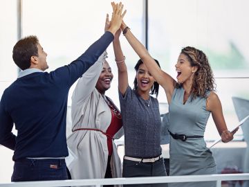 Four colleagues enthusiastically high-five in an office.