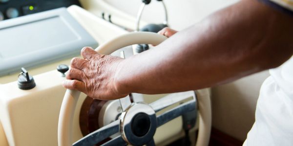 Close-up of a person steering a boat with a white wheel.