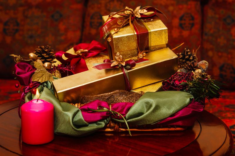 Christmas gifts in gold boxes tied up with decorative ribbons, laid out on a rich rosewood table. Pine cones and other embellishments complete the picture. Horizontal format. Close-up No people. Photo shot with low-key lighting producing rich colour tones.