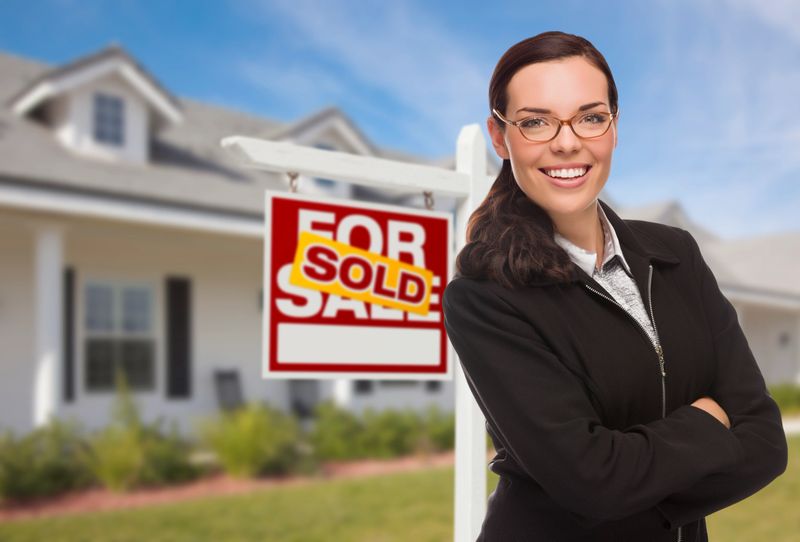 Attractive Mixed Race Woman in Front of House and Sold Real Estate Sign.