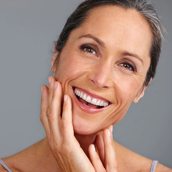Smiling woman with radiant skin touching her face.