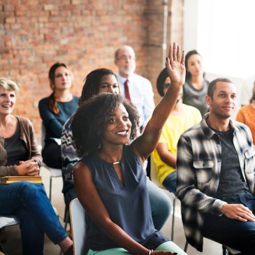 Woman raising hand in a diverse group meeting.