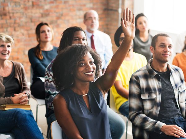 A woman raises her hand during a diverse group meeting or workshop.