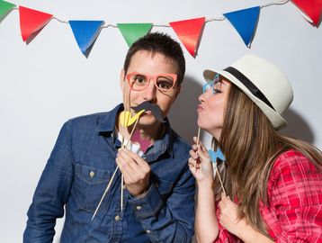 Couple having fun with playful photo booth props and colorful bunting.