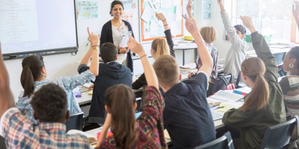 Students raising hands in a classroom answering the teacher's question.