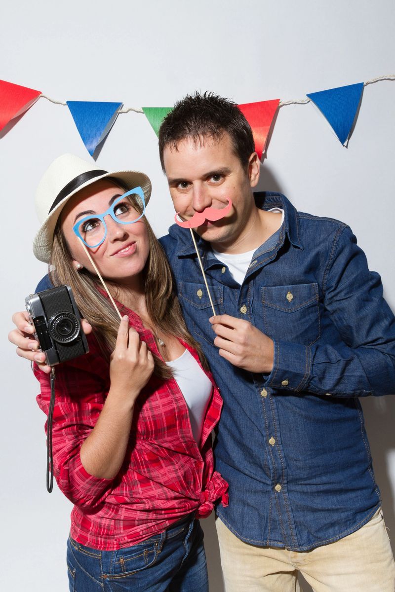Young couple in a Photo Booth party holding fake paper mustache
