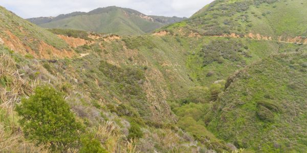 Lush green hills with winding dirt paths under a cloudy sky.