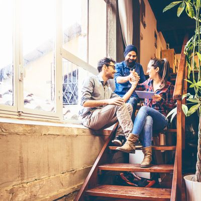 Three friends sitting on stairs, sharing a joyful moment indoors.