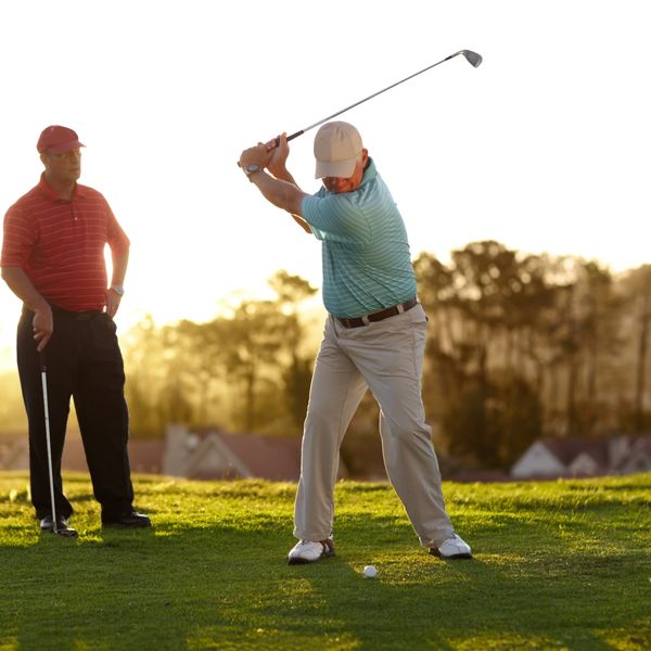 Two men playing golf on a sunny day, one preparing to swing.