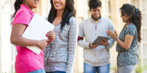Four young adults chatting and smiling outdoors near a building with arches.