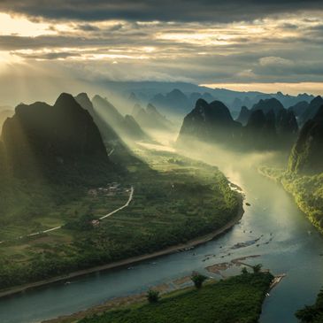 Sunlight beams over a winding river surrounded by karst mountains and lush greenery.