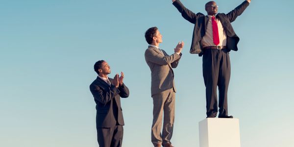 Businessman celebrating on pedestal with others applauding.