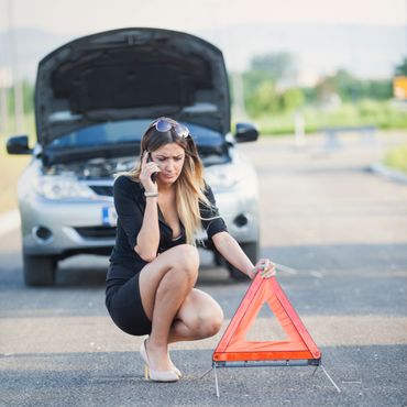 Woman calls for help next to broken down car on roadside.