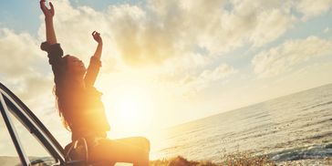 Woman next to ocean with arms raised 